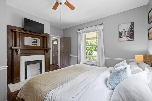 bedroom featuring a ceiling fan, wood finished floors, and a fireplace