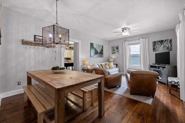 dining space featuring dark wood-type flooring, a textured ceiling, baseboards, and ceiling fan with notable chandelier