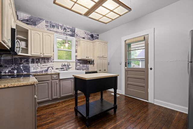 kitchen with baseboards, cream cabinetry, a sink, dark wood finished floors, and backsplash