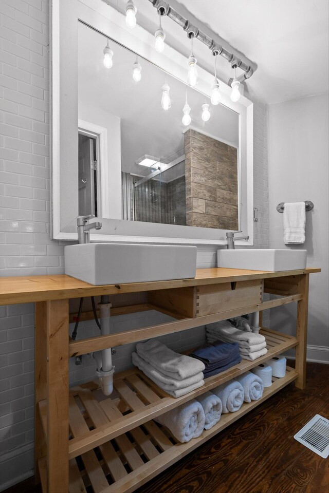 full bath featuring a sink, a shower with door, wood finished floors, and visible vents