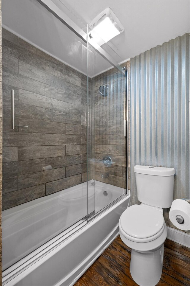 full bathroom with combined bath / shower with glass door, wood finished floors, toilet, and wallpapered walls