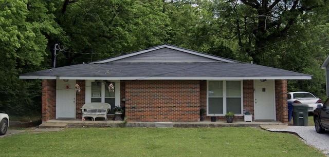 single story home featuring covered porch, a shingled roof, a front lawn, and brick siding