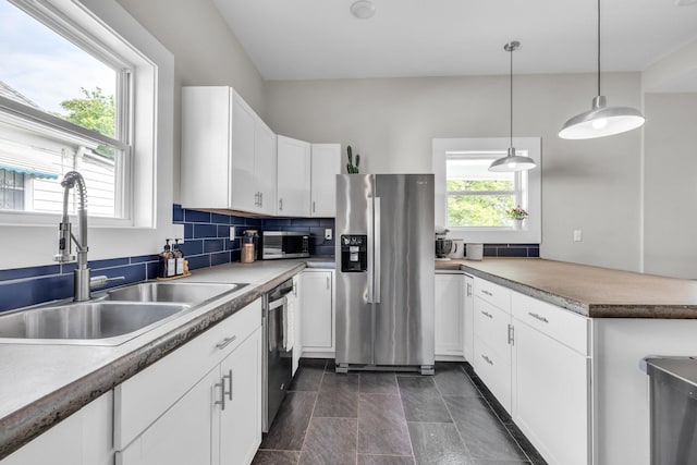 kitchen featuring appliances with stainless steel finishes, hanging light fixtures, a sink, a peninsula, and white cabinetry
