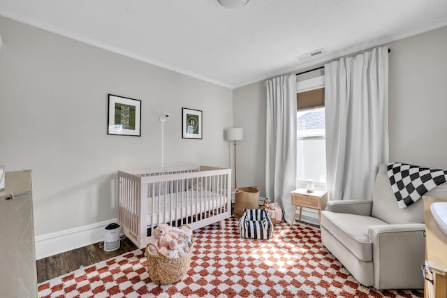 bedroom featuring visible vents, ornamental molding, wood finished floors, baseboards, and a nursery area