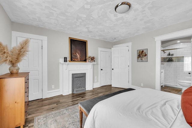 bedroom featuring baseboards, ensuite bath, wood finished floors, and a fireplace