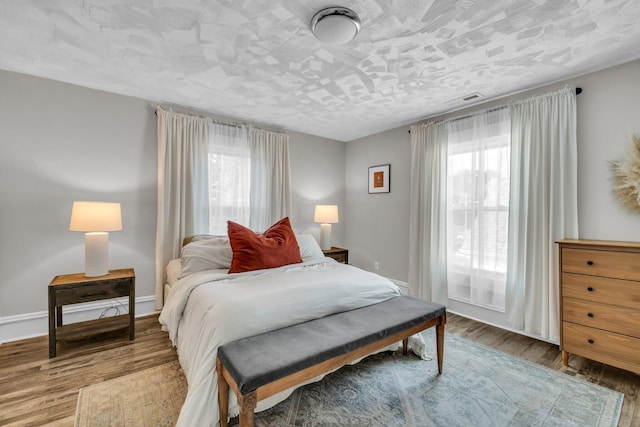 bedroom with visible vents, baseboards, wood finished floors, and multiple windows