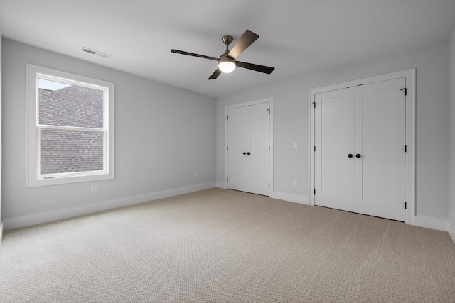 unfurnished bedroom featuring light colored carpet, visible vents, baseboards, and multiple closets