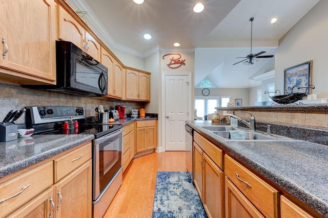kitchen with dark countertops, appliances with stainless steel finishes, a sink, and light wood-type flooring