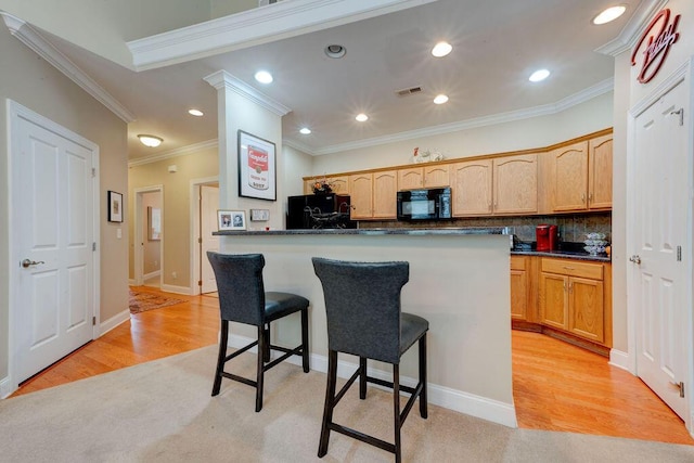 kitchen with crown molding, light wood-style floors, a kitchen breakfast bar, visible vents, and black appliances