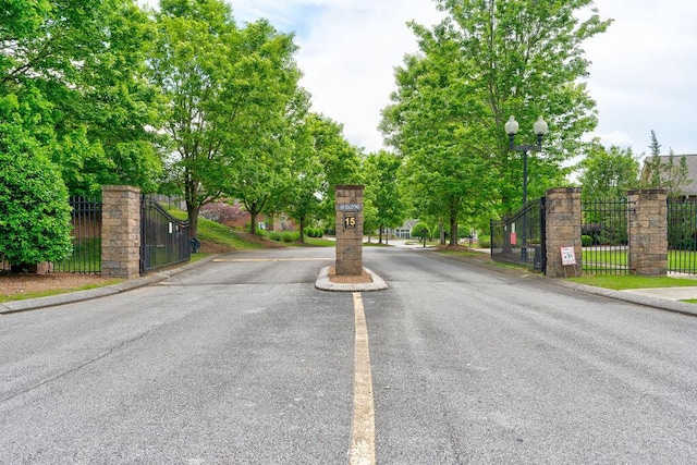 view of street featuring a gate, a gated entry, curbs, and street lights