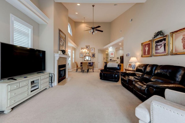 living area featuring a high ceiling, light carpet, ceiling fan with notable chandelier, recessed lighting, and a tile fireplace