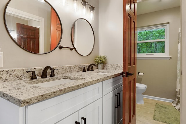 bathroom with toilet, baseboards, double vanity, and a sink