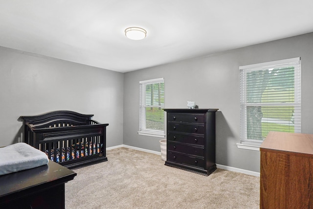 bedroom with baseboards, a nursery area, and carpet