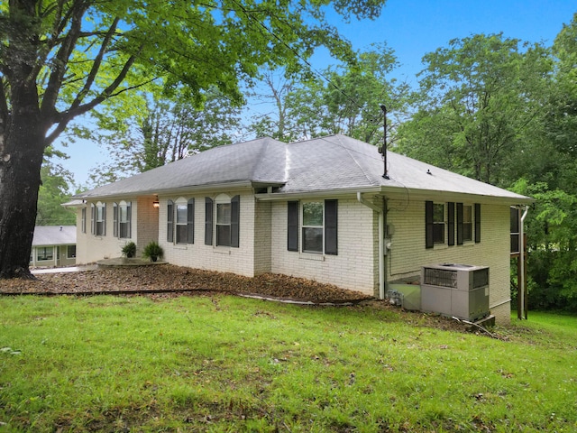view of front of home with central air condition unit, a front yard, roof with shingles, and brick siding