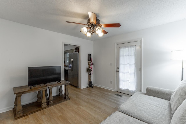 living area with visible vents, light wood-style floors, baseboards, a textured ceiling, and a ceiling fan