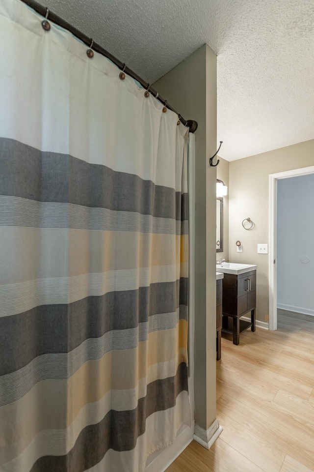 bathroom with vanity, baseboards, a textured ceiling, and wood finished floors