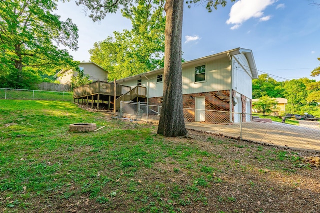 back of property featuring a garage, a fire pit, a wooden deck, a fenced backyard, and a yard