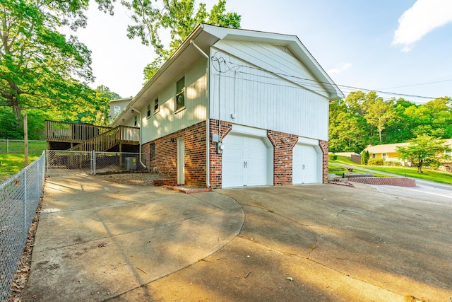 view of property exterior featuring fence, an attached garage, brick siding, a wooden deck, and concrete driveway