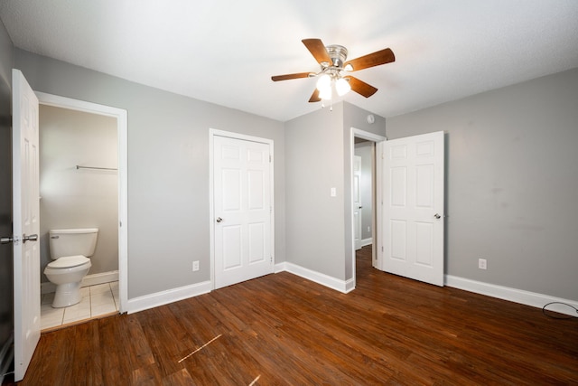 unfurnished bedroom featuring ensuite bath, ceiling fan, baseboards, and wood finished floors