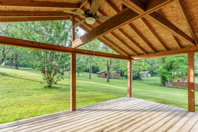 wooden terrace with a lawn, a ceiling fan, and an outbuilding