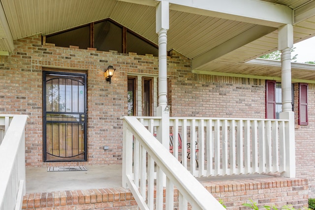 doorway to property featuring covered porch and brick siding