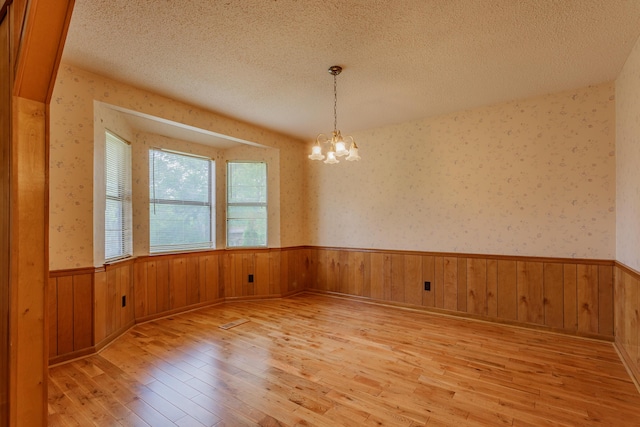 empty room featuring a wainscoted wall, light wood-type flooring, a textured ceiling, and a chandelier