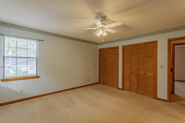 unfurnished bedroom featuring a textured ceiling, multiple closets, light carpet, and baseboards