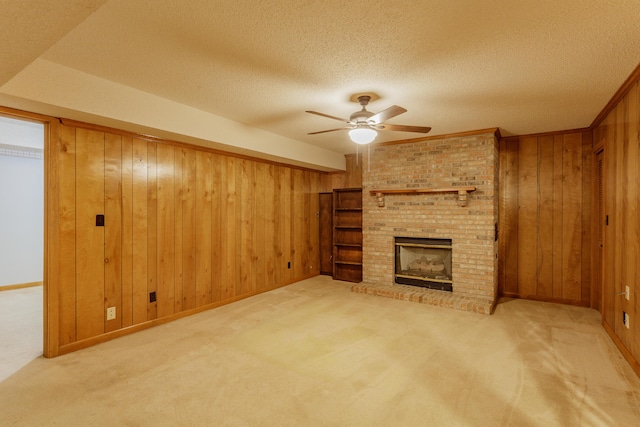 unfurnished living room with a brick fireplace, a textured ceiling, wood walls, carpet, and a ceiling fan
