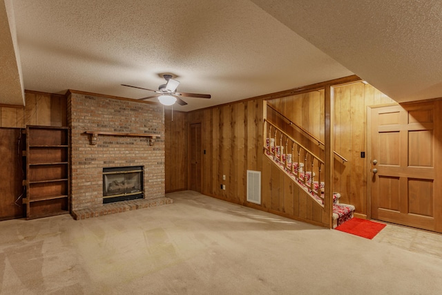 unfurnished living room featuring wooden walls, carpet floors, stairs, and a textured ceiling