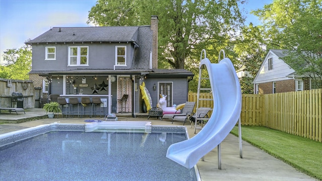 back of house featuring a chimney, fence, outdoor dry bar, and a fenced in pool
