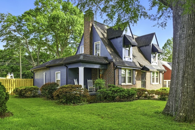 view of side of home featuring a porch, a chimney, brick siding, fence, and a yard