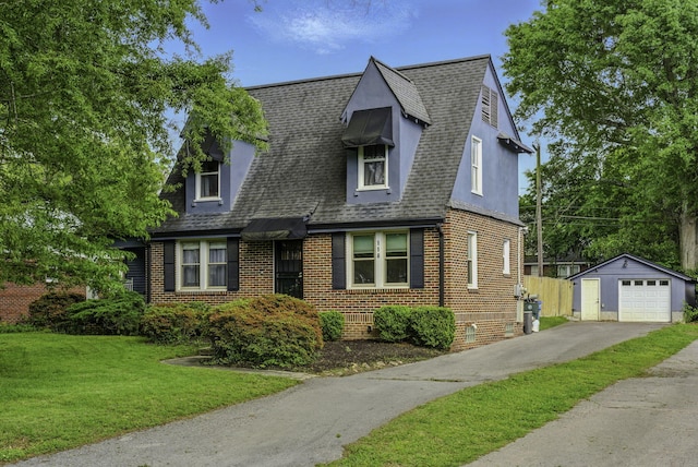 view of front facade featuring an outbuilding, a shingled roof, a front yard, and aphalt driveway