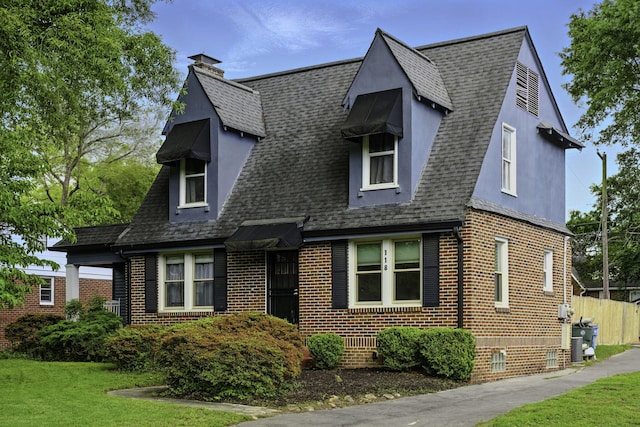 cape cod-style house featuring roof with shingles, a chimney, a front lawn, and brick siding