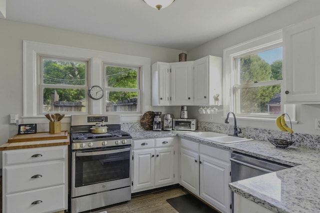 kitchen featuring light stone countertops, dark wood finished floors, a sink, stainless steel appliances, and white cabinetry