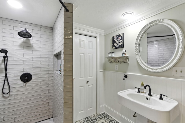 bathroom featuring ornamental molding, wainscoting, tiled shower, a textured ceiling, and a sink