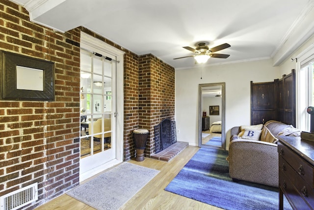 living area featuring visible vents, ceiling fan, wood finished floors, and brick wall