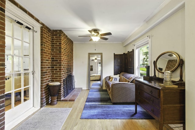 interior space with crown molding, a brick fireplace, a ceiling fan, baseboards, and wood finished floors