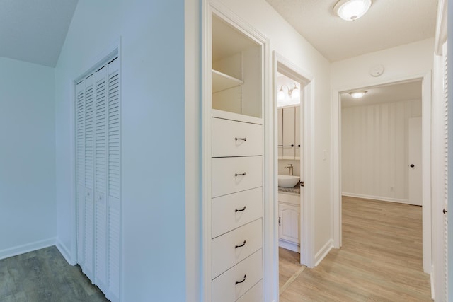 corridor featuring light wood-style floors, a sink, and baseboards