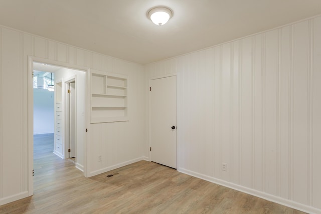 spare room featuring baseboards, visible vents, built in shelves, and light wood-style floors