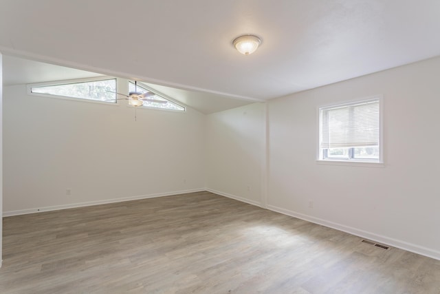 empty room featuring visible vents, baseboards, a ceiling fan, light wood-style flooring, and vaulted ceiling