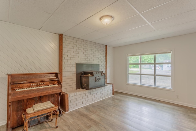 living room with baseboards, a wood stove, a drop ceiling, and wood finished floors