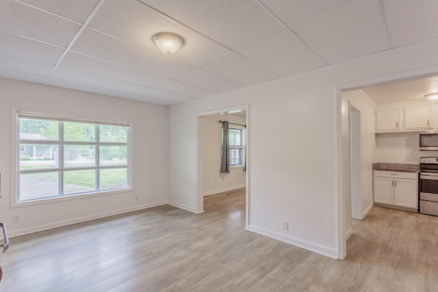 interior space with light wood-type flooring, a paneled ceiling, and baseboards