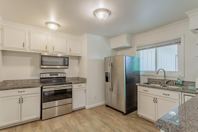 kitchen featuring crown molding, a sink, dark stone countertops, stainless steel appliances, and white cabinetry