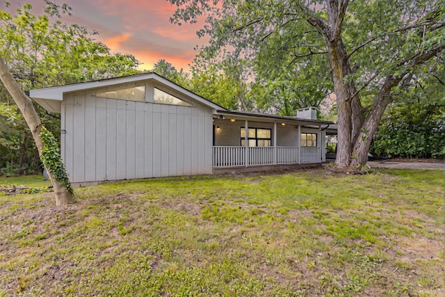 rear view of property featuring a lawn, covered porch, and a chimney