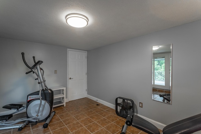 exercise area with a textured ceiling, baseboards, and dark tile patterned floors