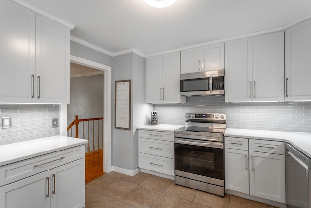 kitchen with light countertops, stainless steel appliances, light tile patterned floors, backsplash, and ornamental molding