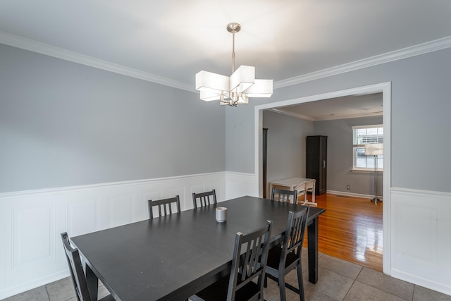 tiled dining space featuring crown molding, wainscoting, and an inviting chandelier