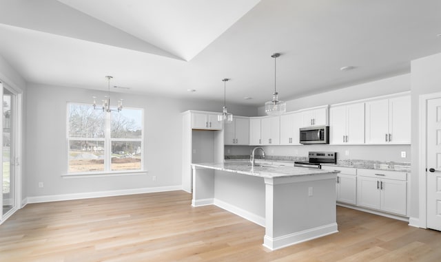 kitchen with appliances with stainless steel finishes, a sink, white cabinetry, light stone countertops, and light wood-style floors