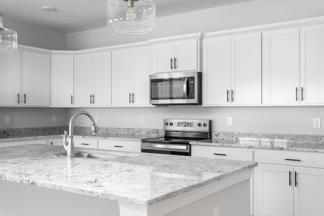 kitchen with appliances with stainless steel finishes, a sink, a kitchen island with sink, and white cabinetry