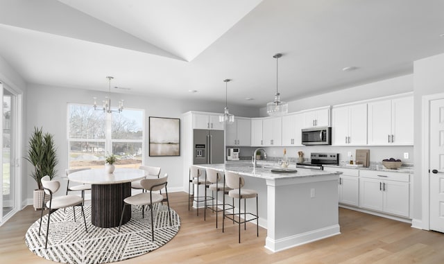 kitchen featuring appliances with stainless steel finishes, a sink, white cabinets, light wood-style flooring, and lofted ceiling